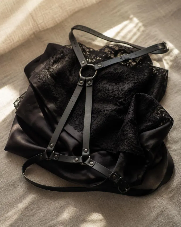 Schwarzes Lederharness neben Spitze auf dunklem Satin im warmen Licht